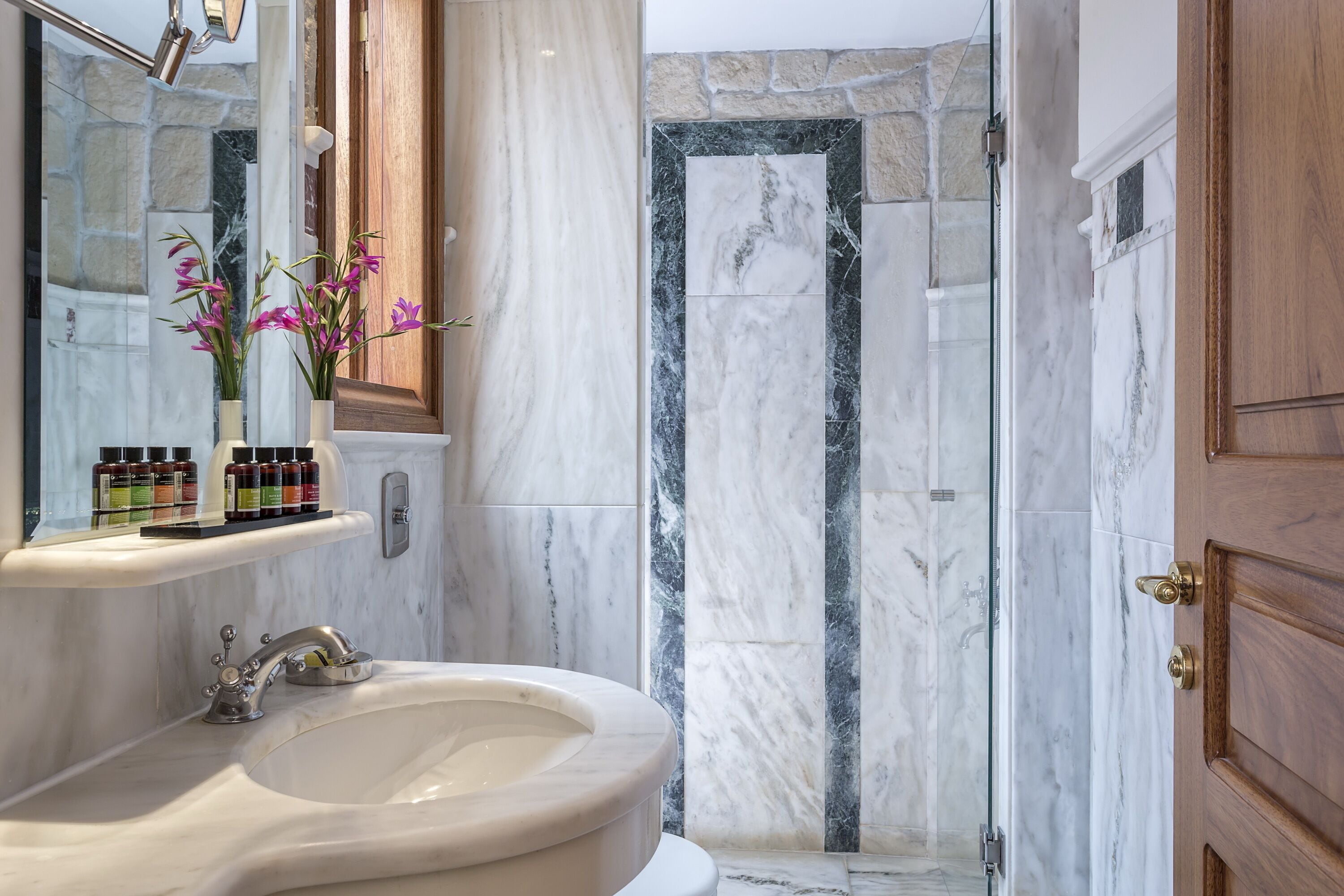 A bathroom with a marble sink, a mirror, and a shower area with stone walls.