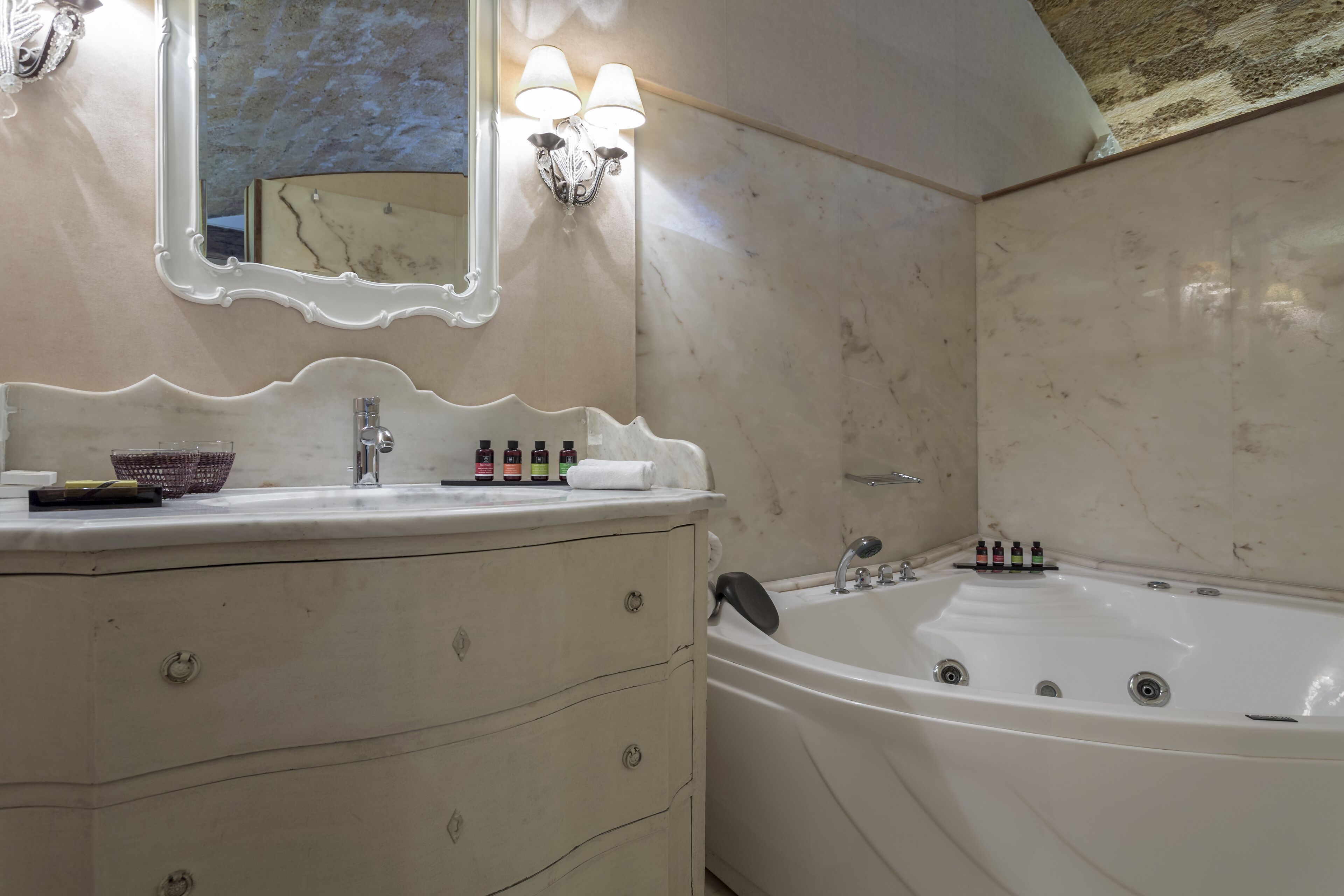 Une salle de bain dotée d’un meuble-lavabo en marbre, d’une grande baignoire et d’un miroir mural agrémenté d’appliques.