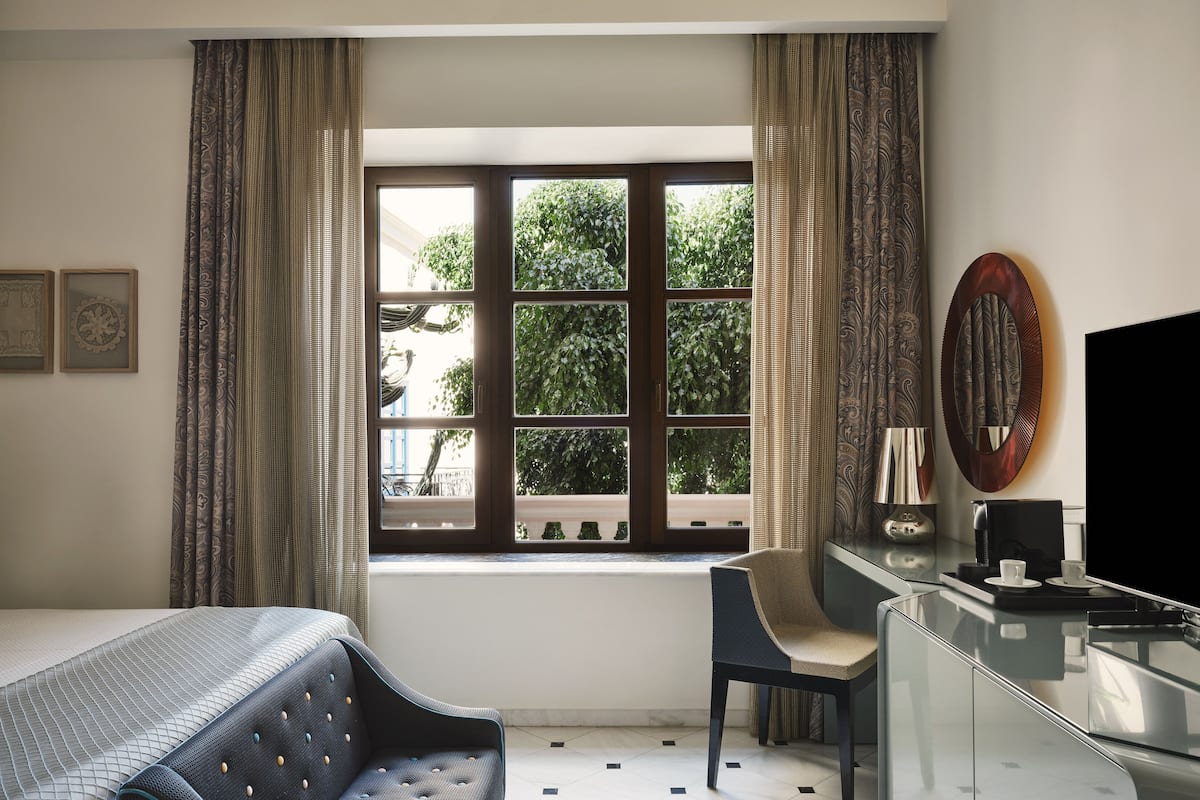 Ein Hotelzimmer mit einem Bett, einem Schreibtisch, einem Stuhl und einem großen Fenster mit Vorhängen.