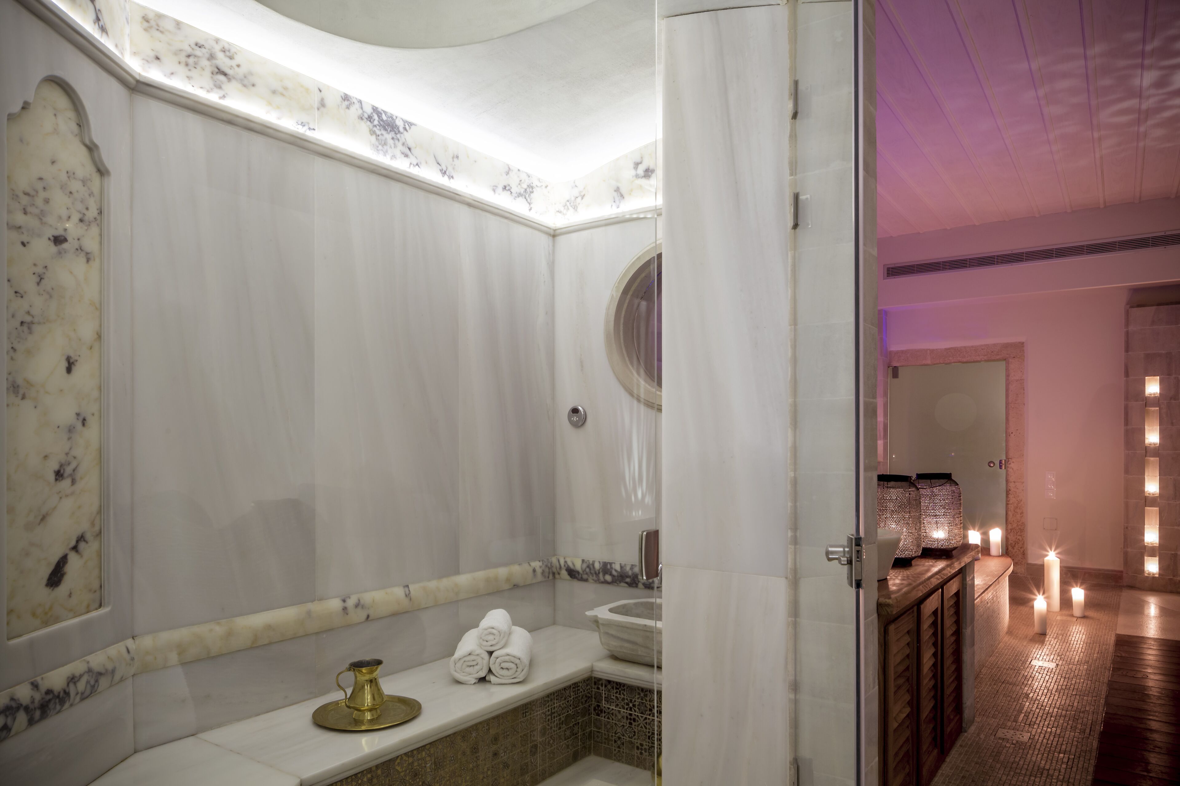 A bathroom with a marble wall, a sink, a mirror, and a towel rack.