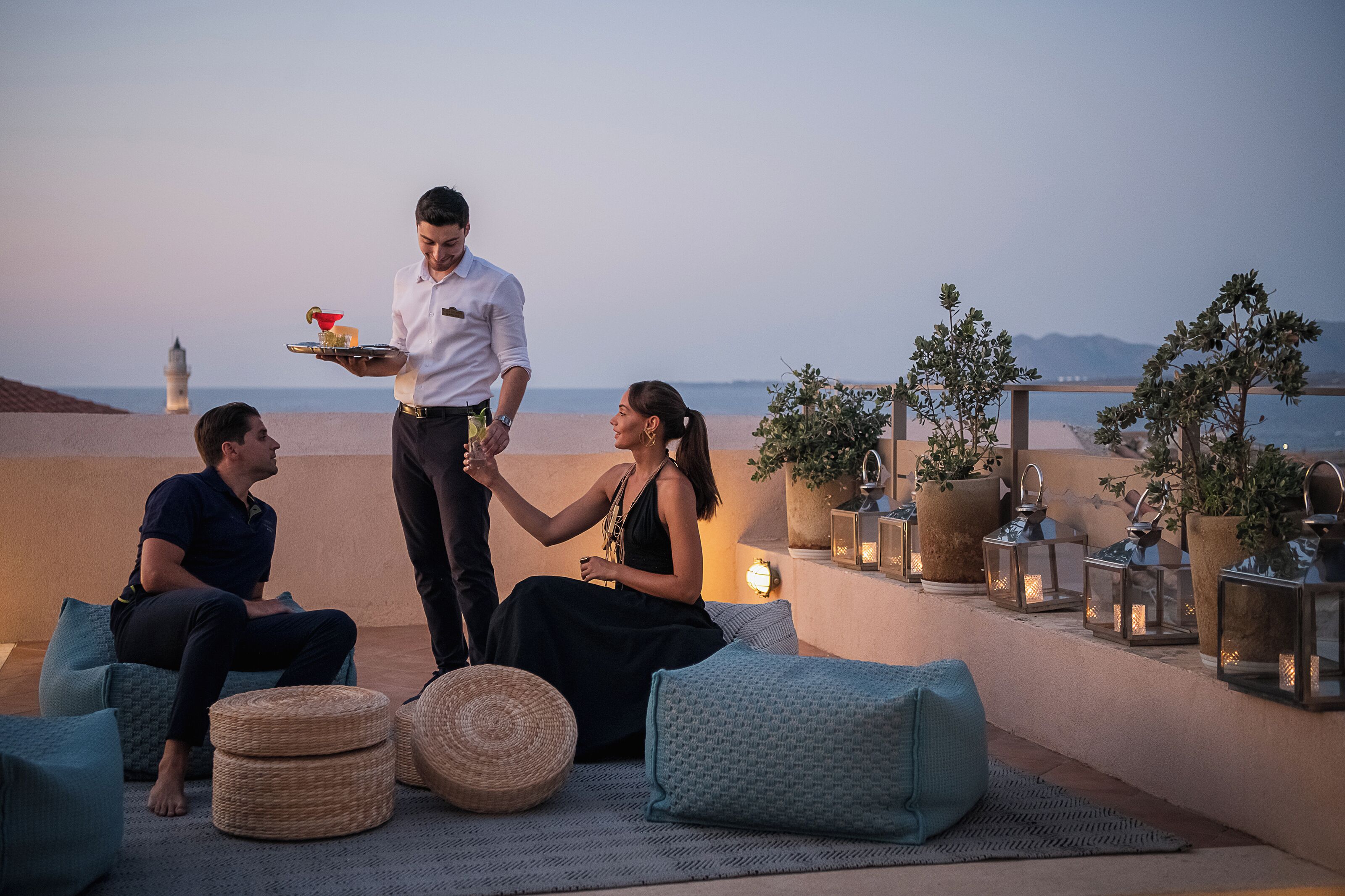 A rooftop terrace with seating, potted plants, and a view of the sea.