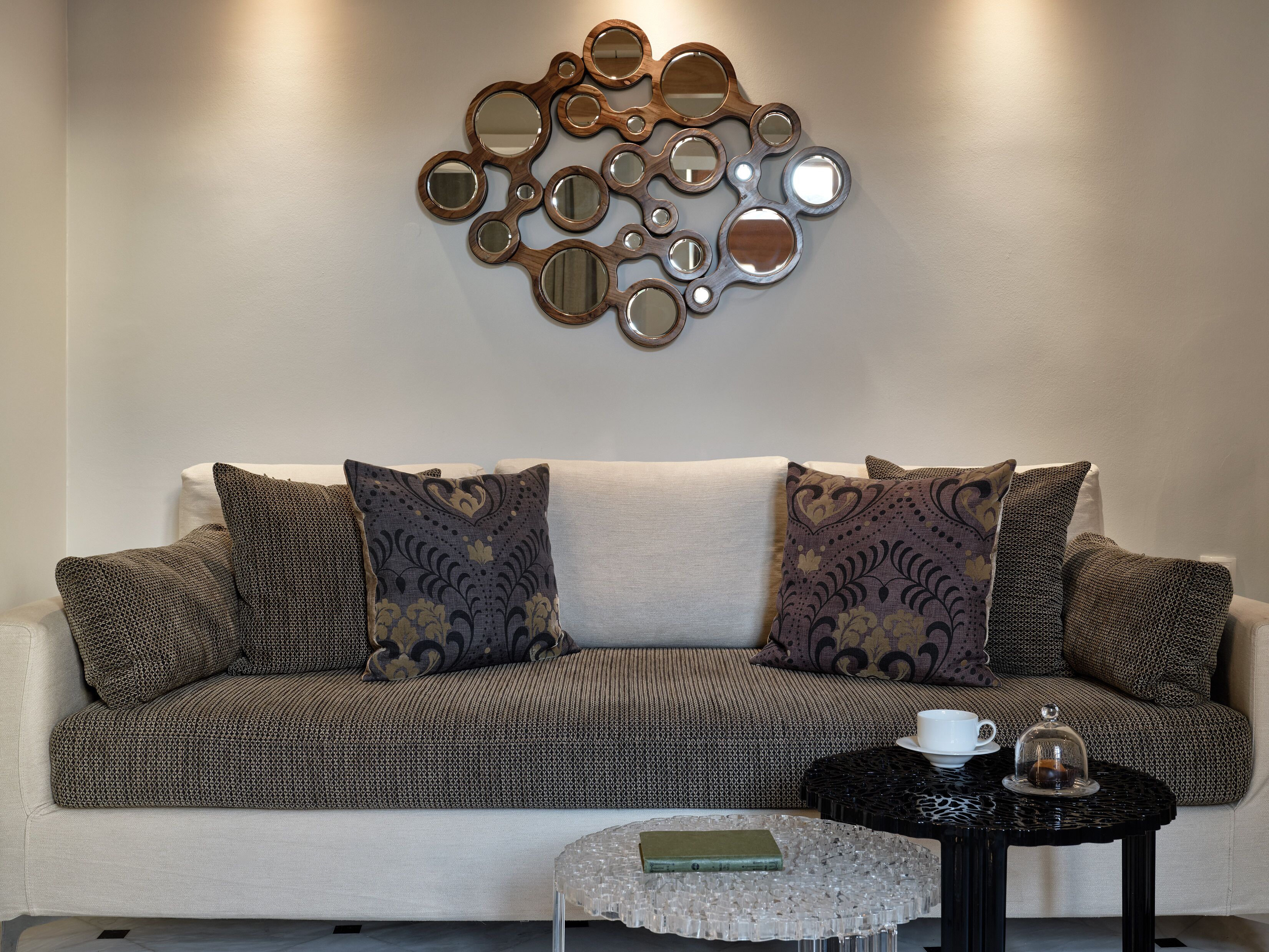 A living room with a patterned sofa, decorative wall mirrors, a small round coffee table, and a white cup.