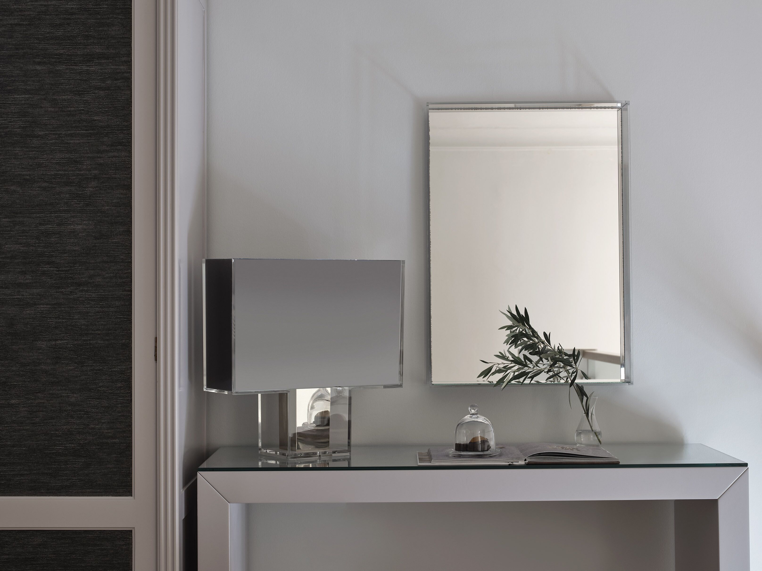A modern, minimalist desk with a glass top, a white cabinet, and a large mirror.