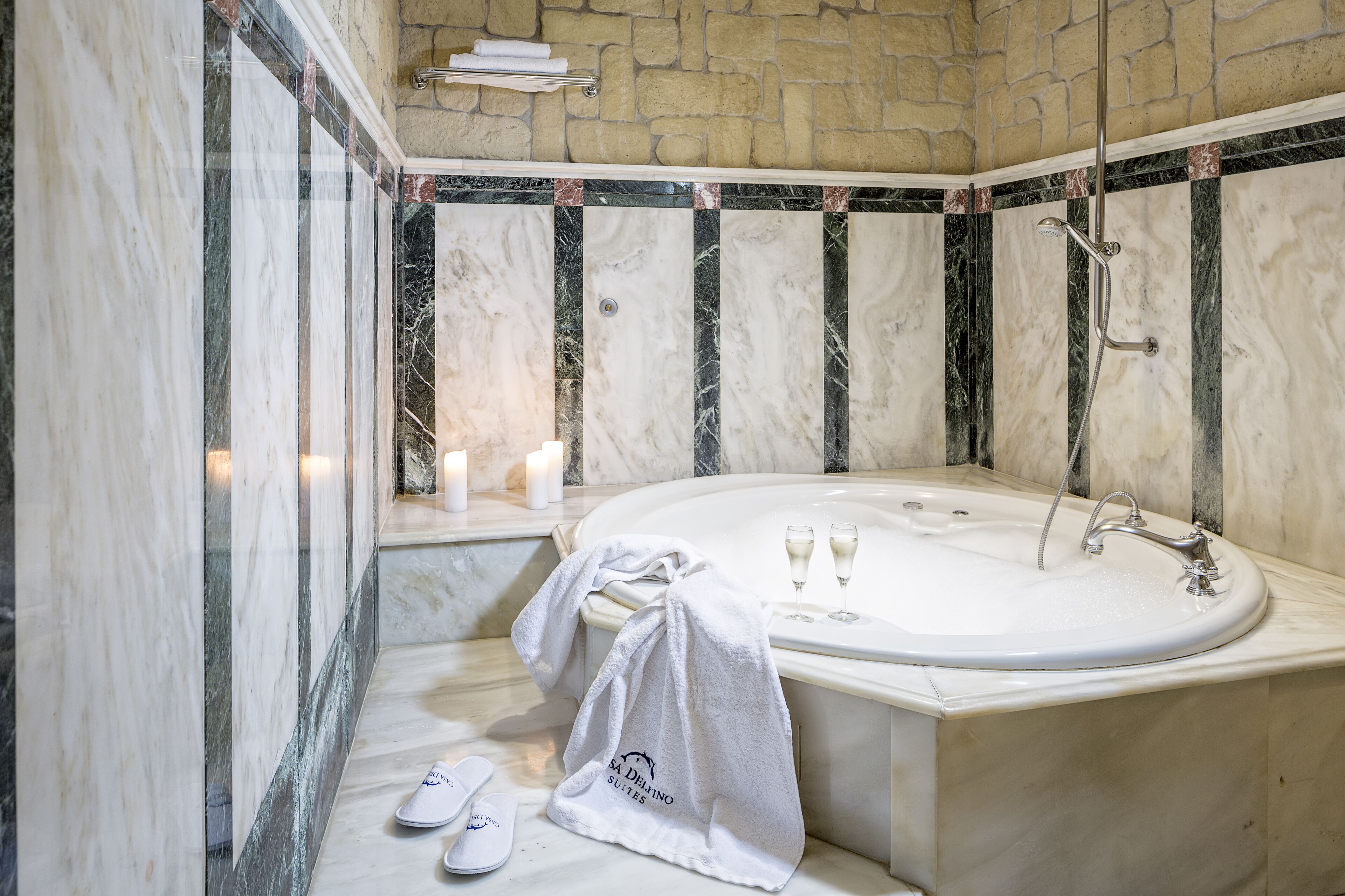 A bathroom with a marble wall, a bathtub, and a towel on the floor.