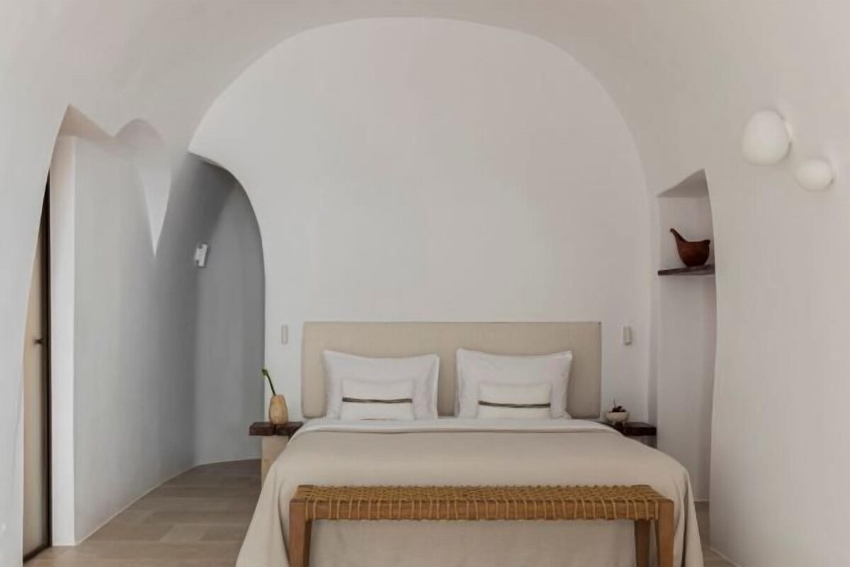 Un dormitorio con una cama, mesitas de noche, una mesilla auxiliar y una estantería en la pared.