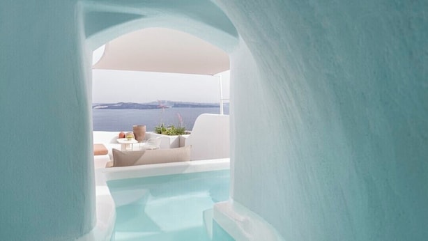 A modern, minimalist indoor pool area with a clear view of the ocean and a white outdoor seating area.