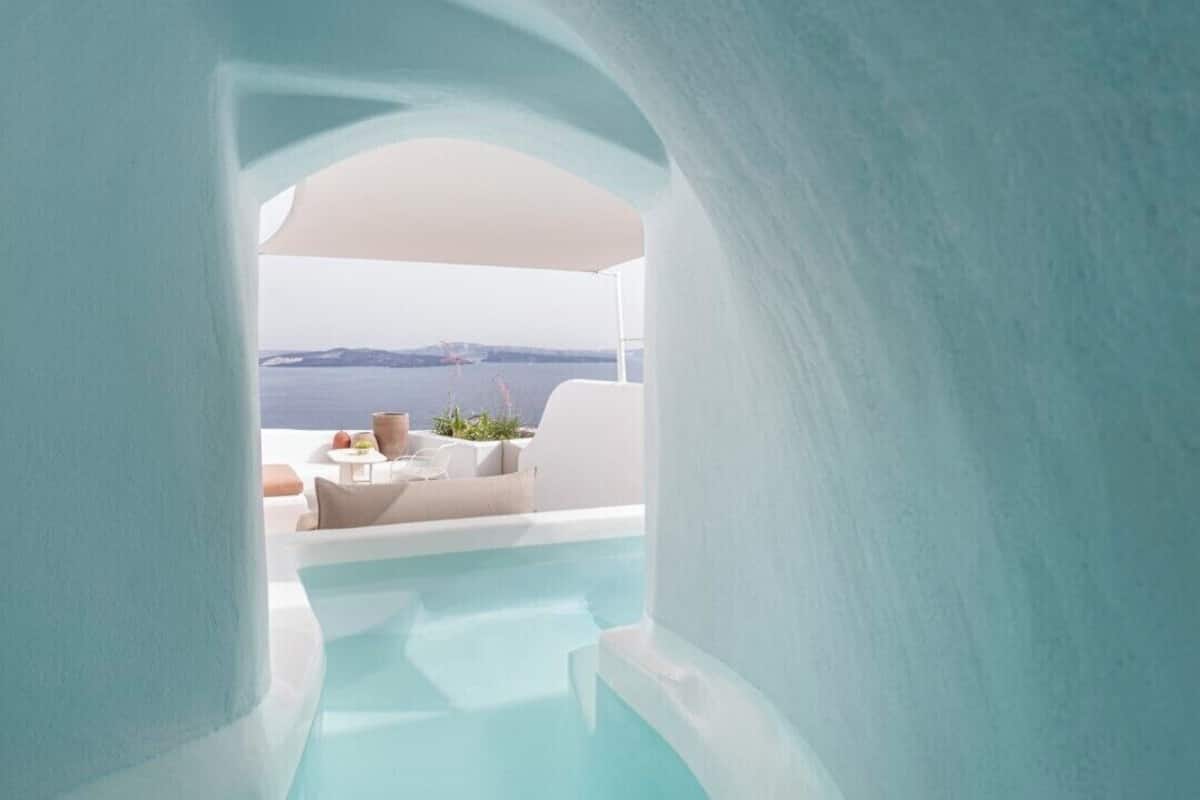 A modern, minimalist indoor pool area with a clear view of the ocean and a white outdoor seating area.