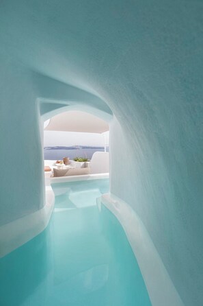 Un área de piscina interior moderna y minimalista, con vista despejada al océano y un área de estar exterior en blanco.