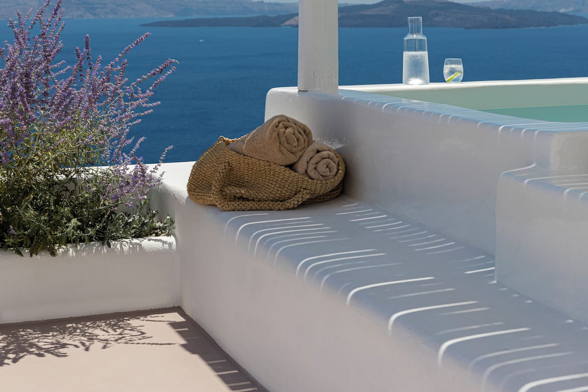 A white outdoor seating area with a view of the sea and distant hills.