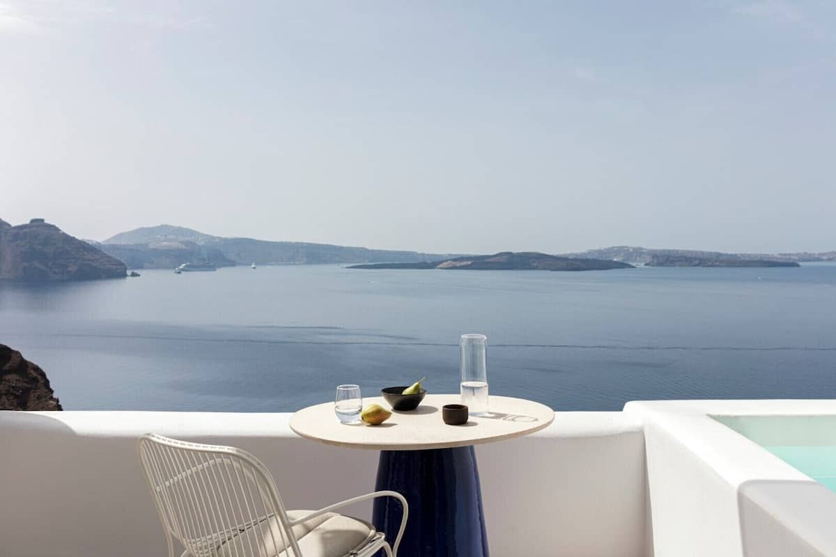 A table with a view of a calm sea and distant islands, a chair, and a glass of water.