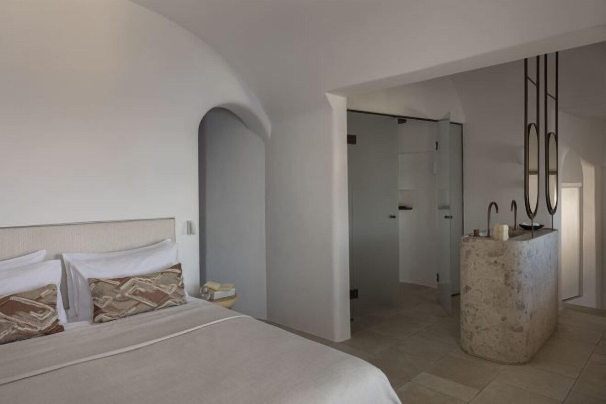 Un dormitorio con cama, mesita de noche y baño visible a través de una puerta abierta.
