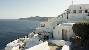 A white building with a sign reading "CANAVES ENA" on a coastal cliff overlooking the sea.