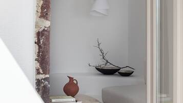 Habitación minimalista con pared blanca, mesa de madera con libros, un jarrón marrón y una rama en un cuenco negro.