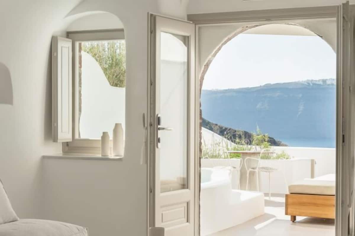 A room with a view of the sea, a balcony with outdoor furniture, and a large arched doorway.