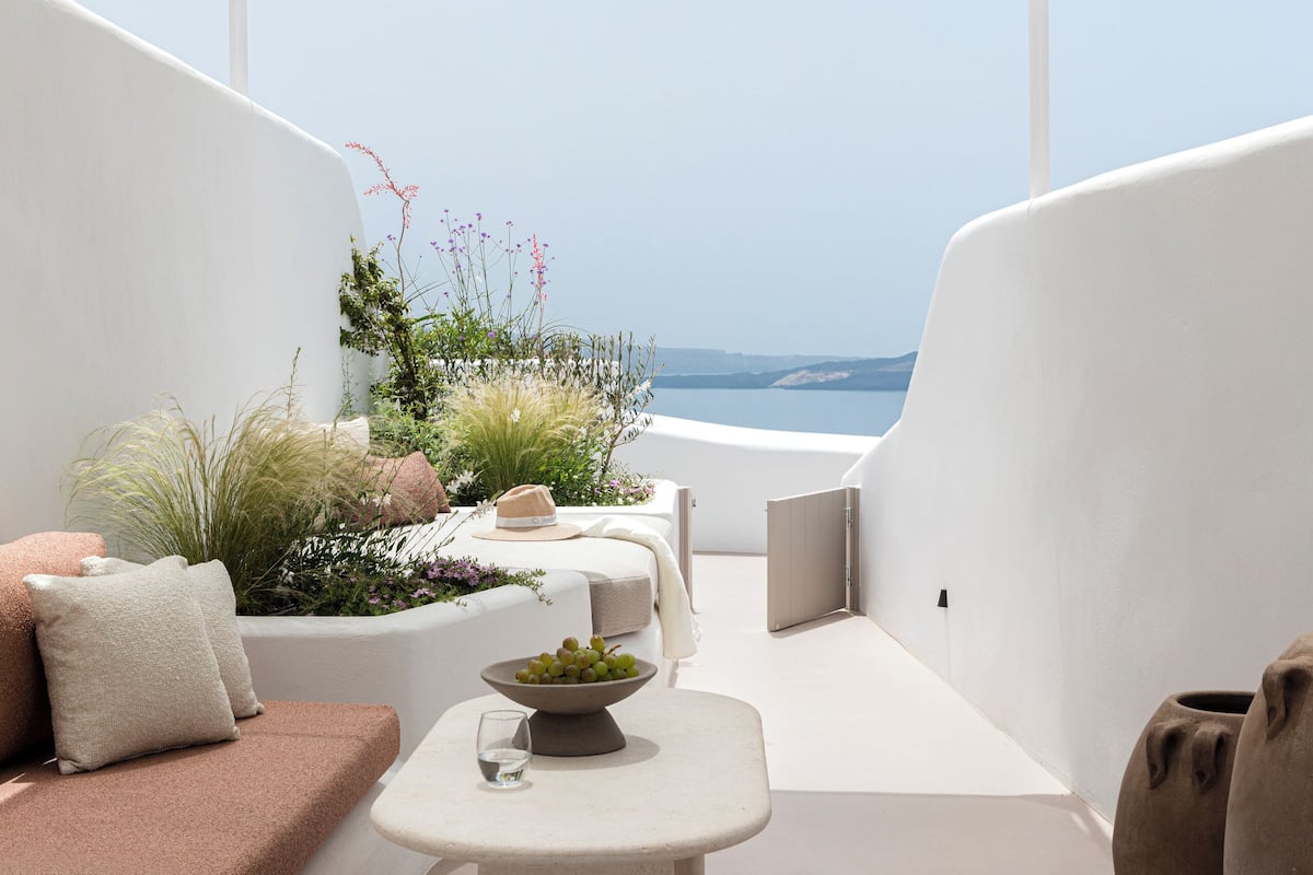 A sunlit outdoor seating area with a table, cushions, and a view of the sea.