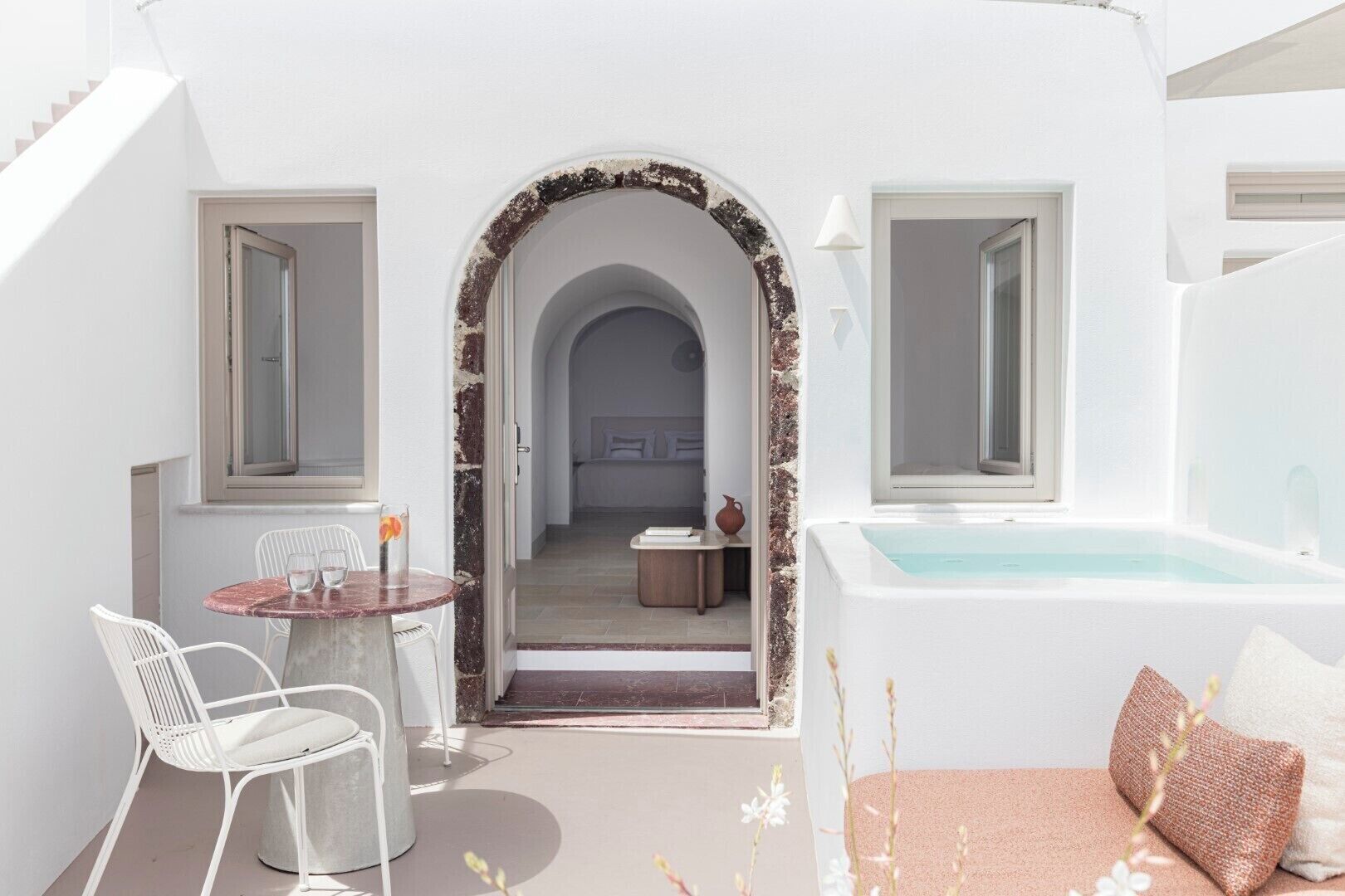 A modern, minimalist outdoor area with a round table, white chairs, a small seating area, and a hot tub.