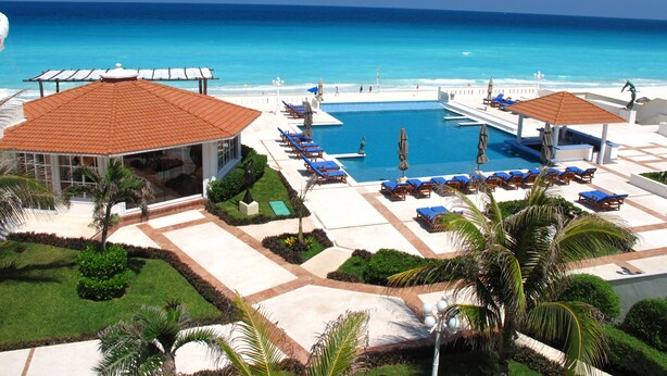 Un resort con piscina, sillas de descanso y vista al océano.