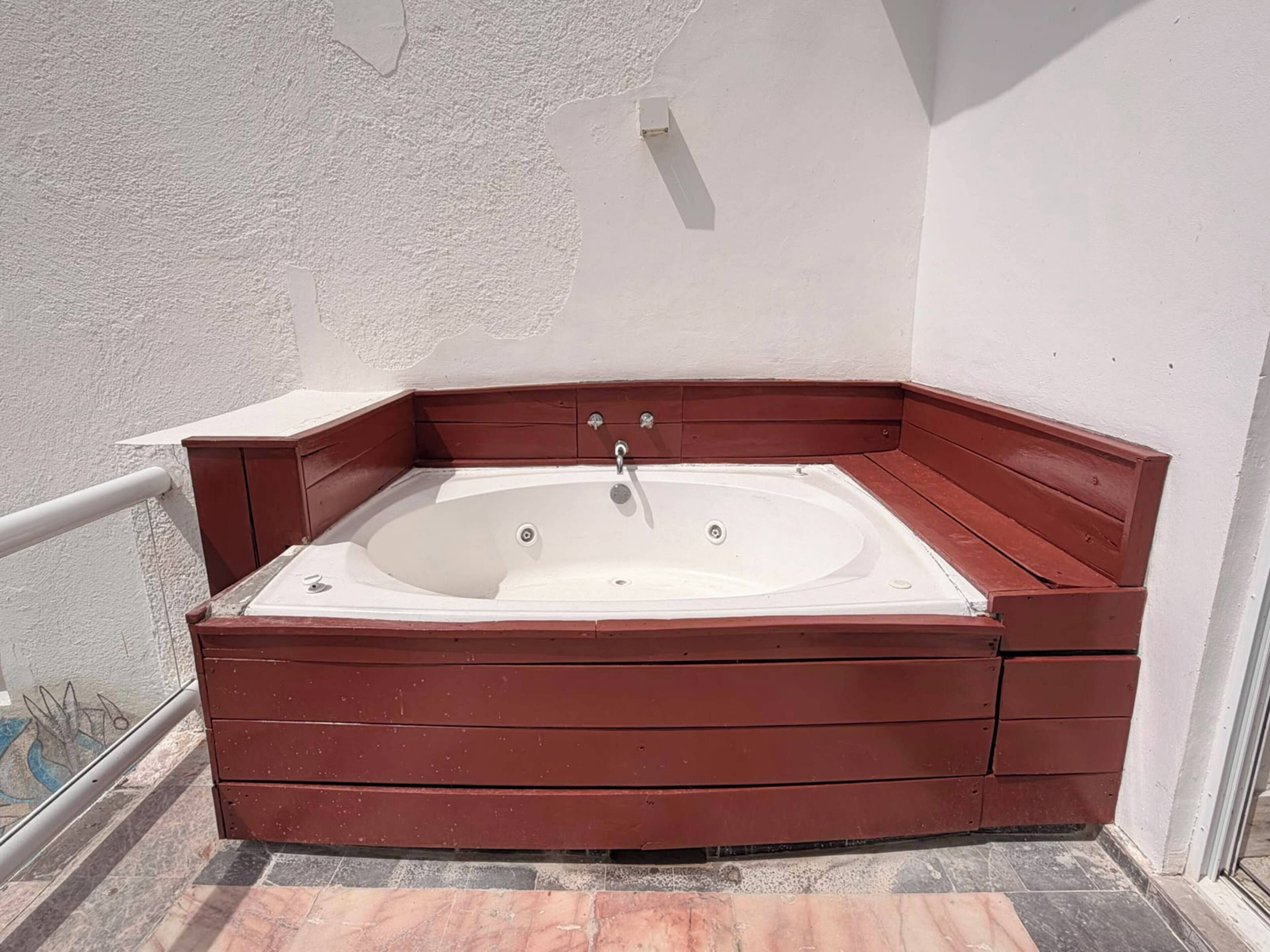 A corner bathtub with wooden panels, a white wall, and a tiled floor.