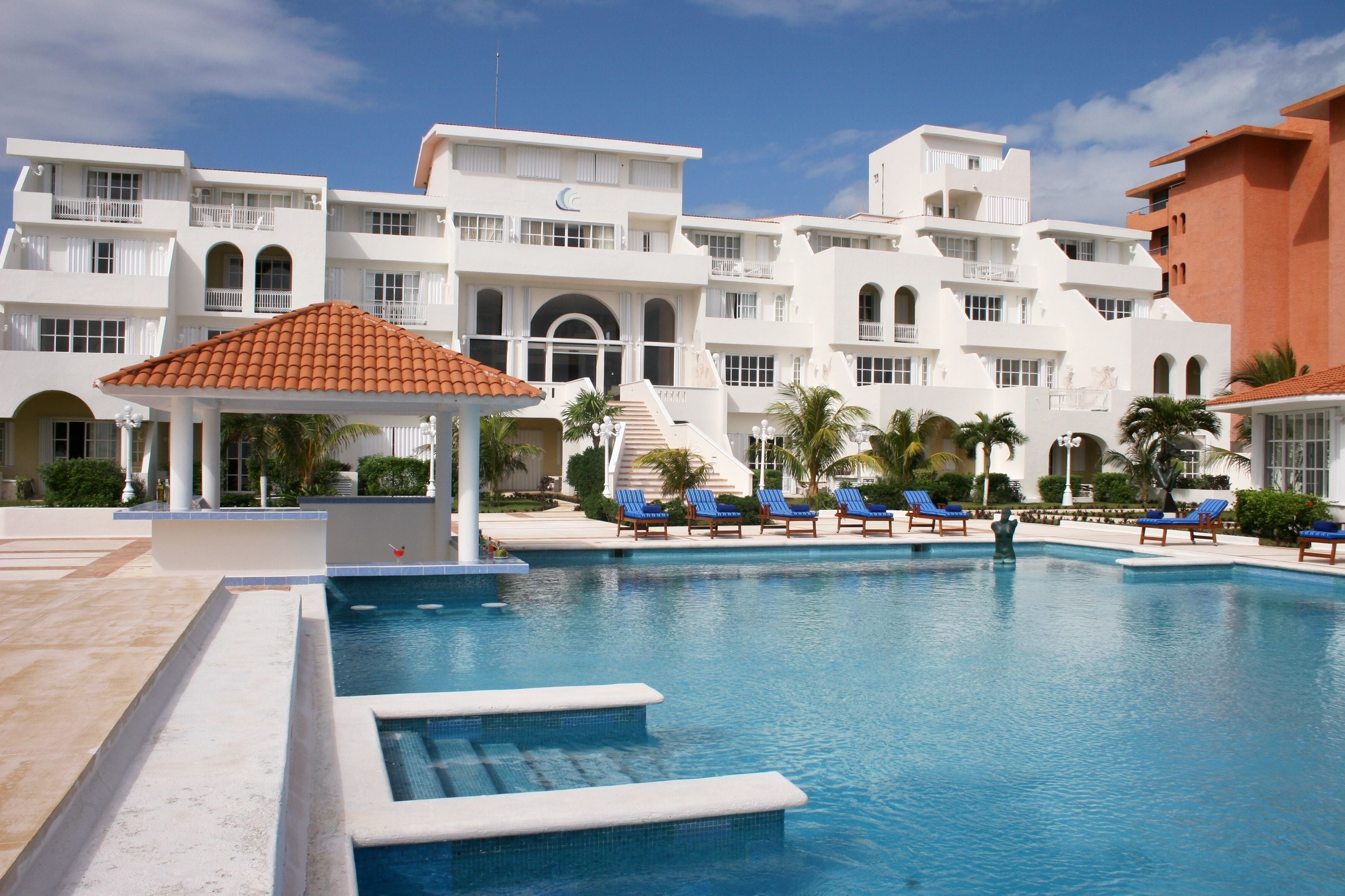 A swimming pool with lounge chairs, a gazebo, and a building with multiple balconies.