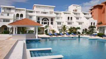 A swimming pool with lounge chairs, a gazebo, and a building with multiple balconies.