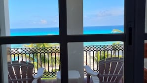 Vista desde una habitación con un ventanal grande que da a un balcón con sillas y barandilla.