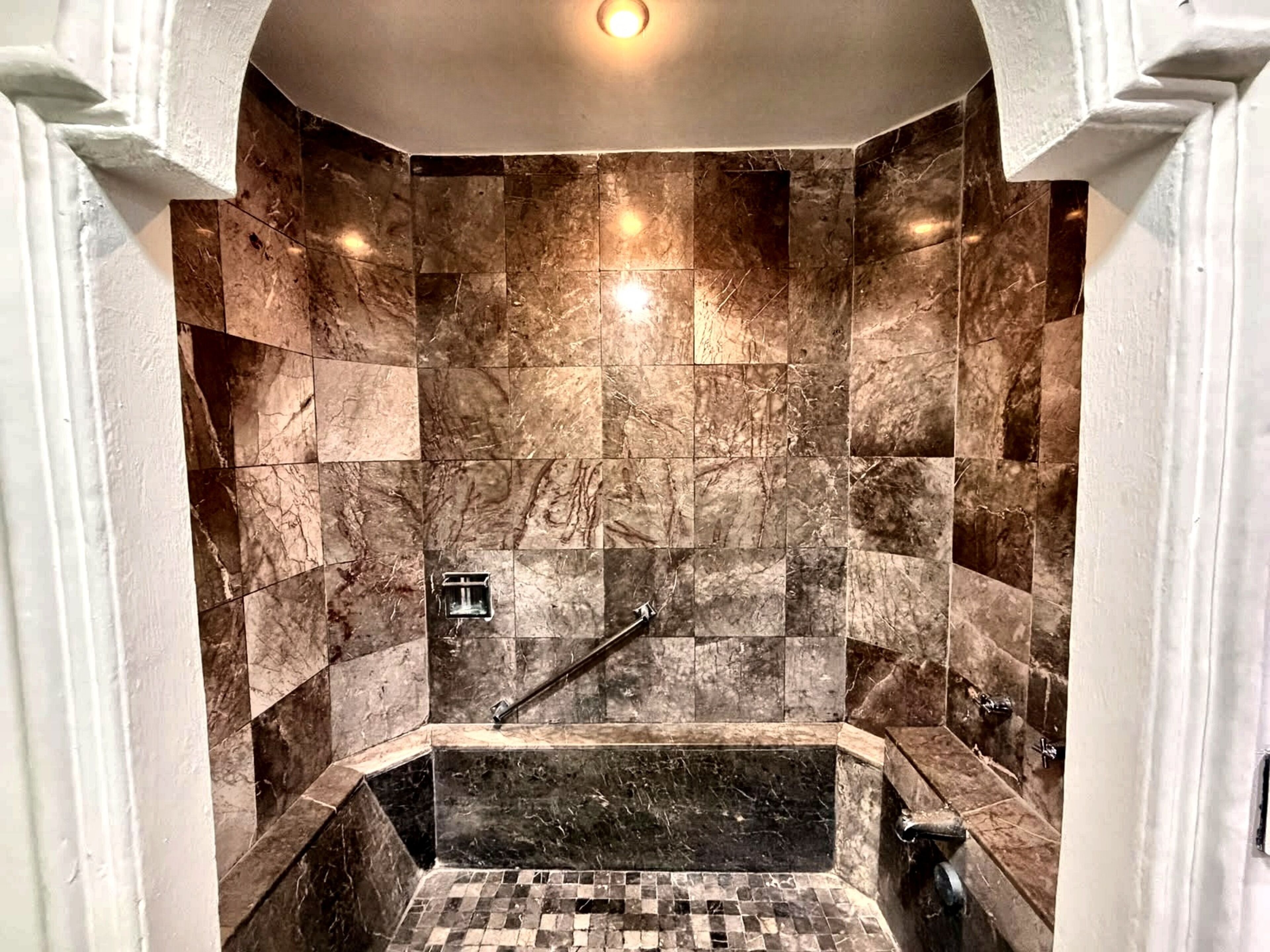 A modern bathroom with a marble shower wall, a built-in bathtub, and a handrail.