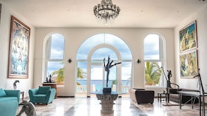 Una habitación amplia con un gran ventanal arqueado, un candelabro y una estatua sobre un pedestal.