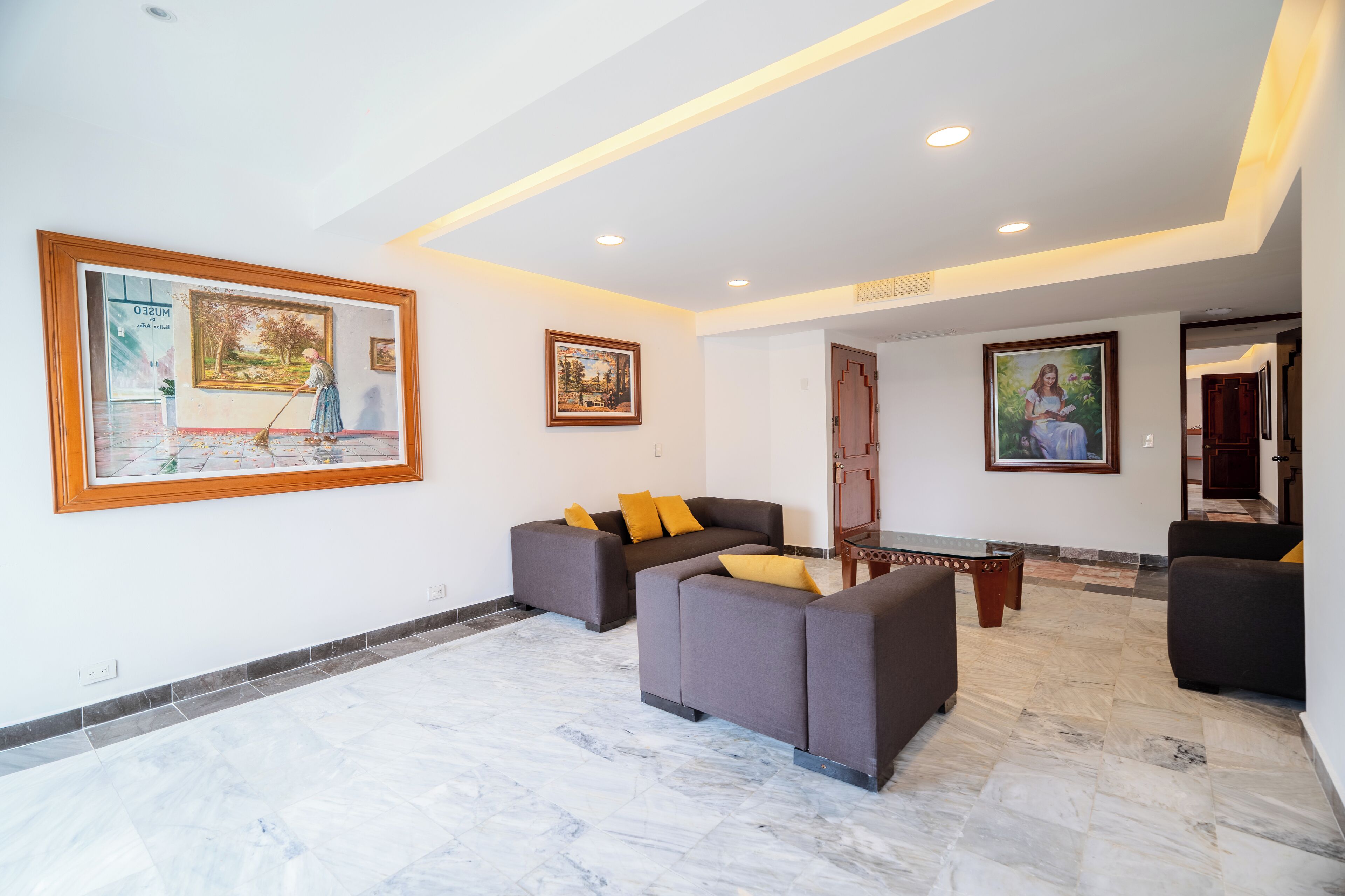 A spacious living area with a large sofa set, a coffee table, and artwork on the walls.