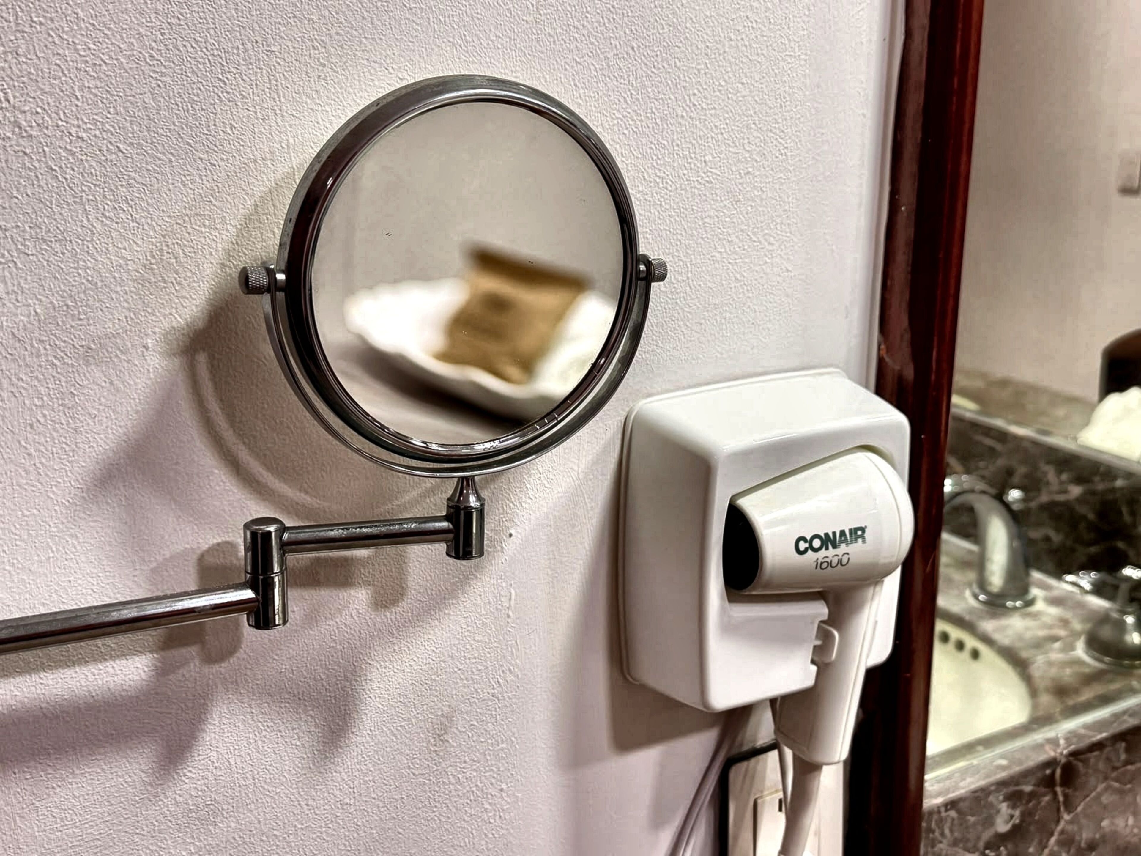 Ein Badezimmer mit einem an der Wand befestigten Spiegel, einem Handtuchhalter und einem Händetrockner.