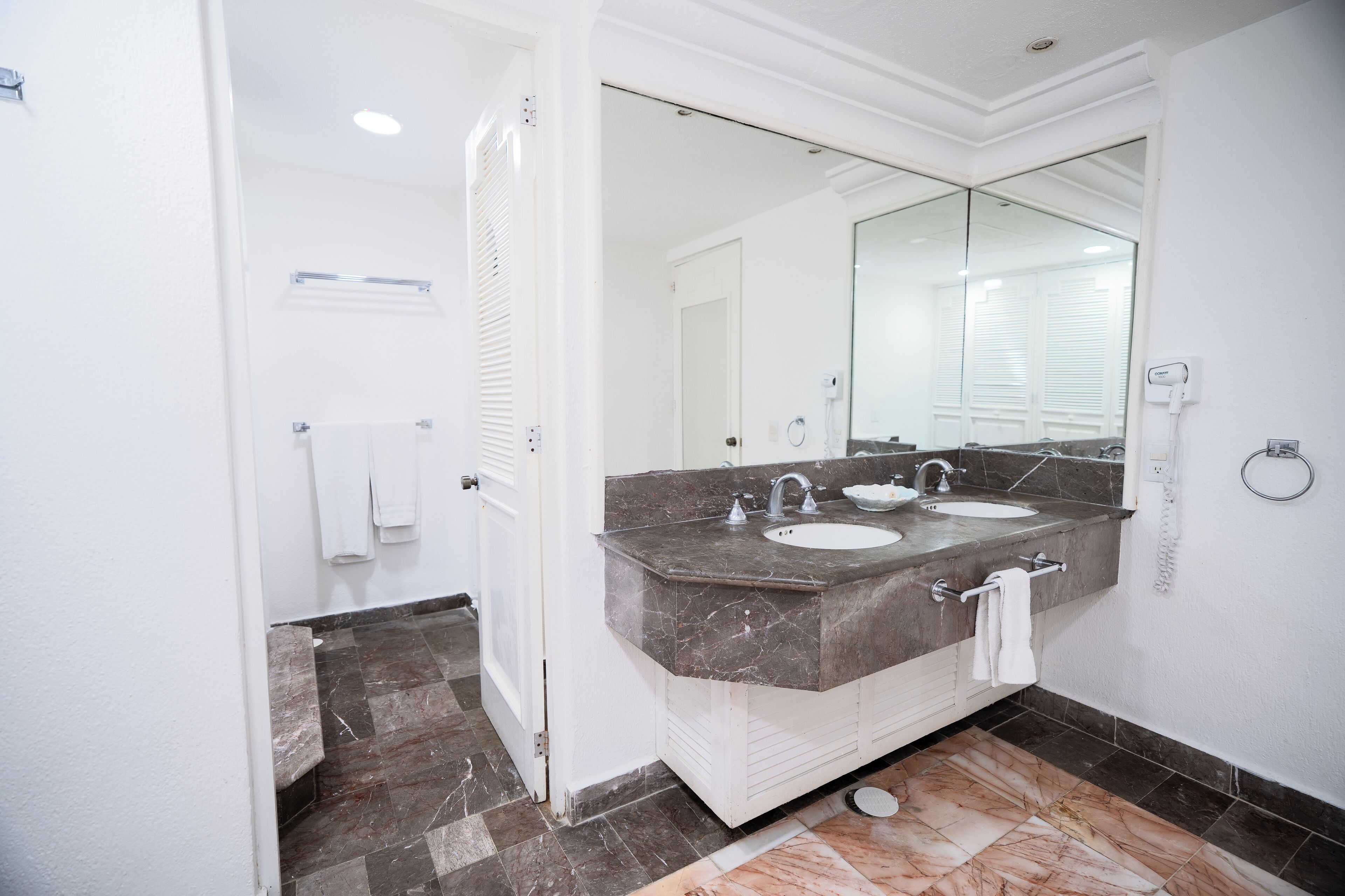 A bathroom with two sinks, a large mirror, and a hairdryer on the wall.
