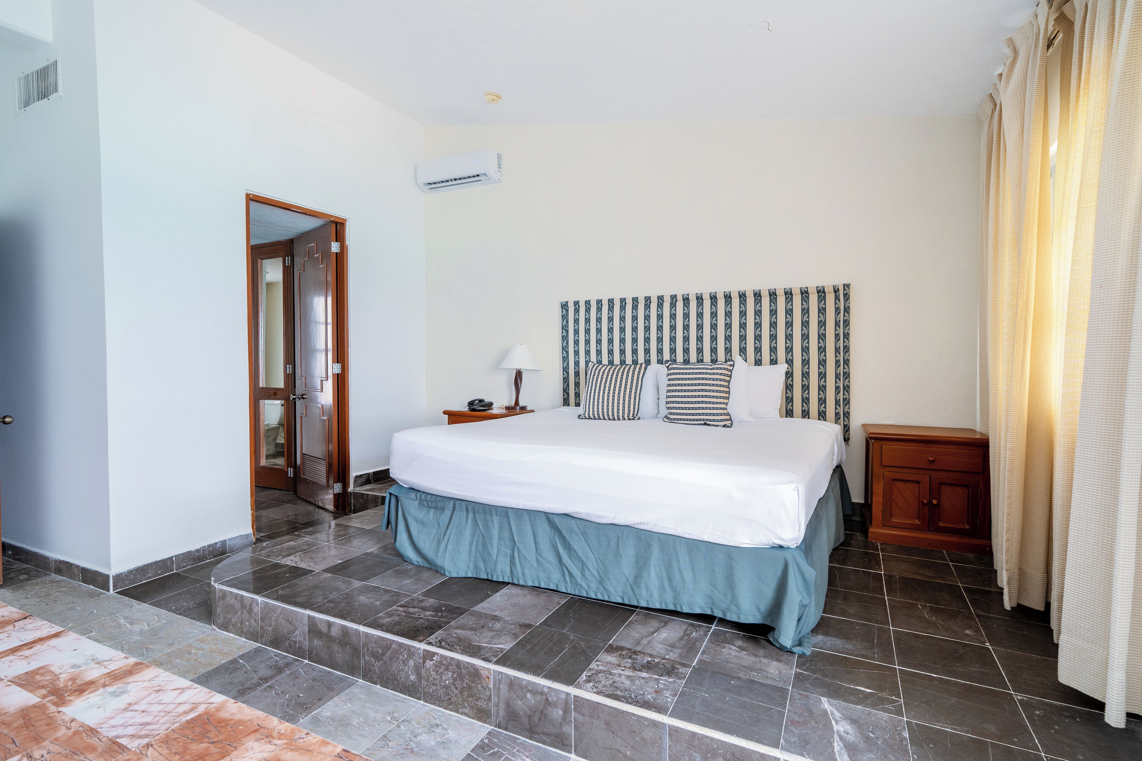 A bedroom with a bed, a nightstand, a lamp, a wooden cabinet, and a door.