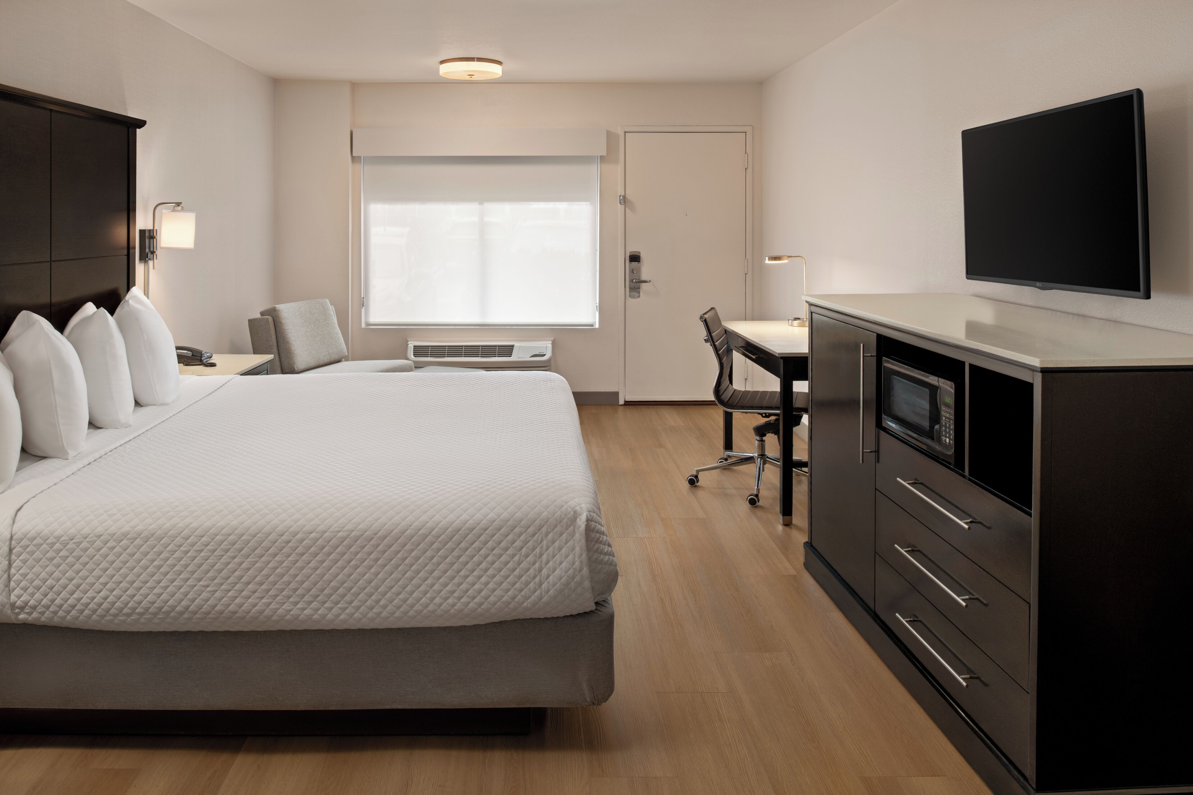 Habitación de hotel con cama, escritorio, televisor y armario.