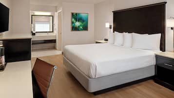 A hotel room with a bed, bedside table, desk, chair, and a television.