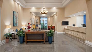 A hotel lobby with a reception desk, seating area, and a large chandelier.