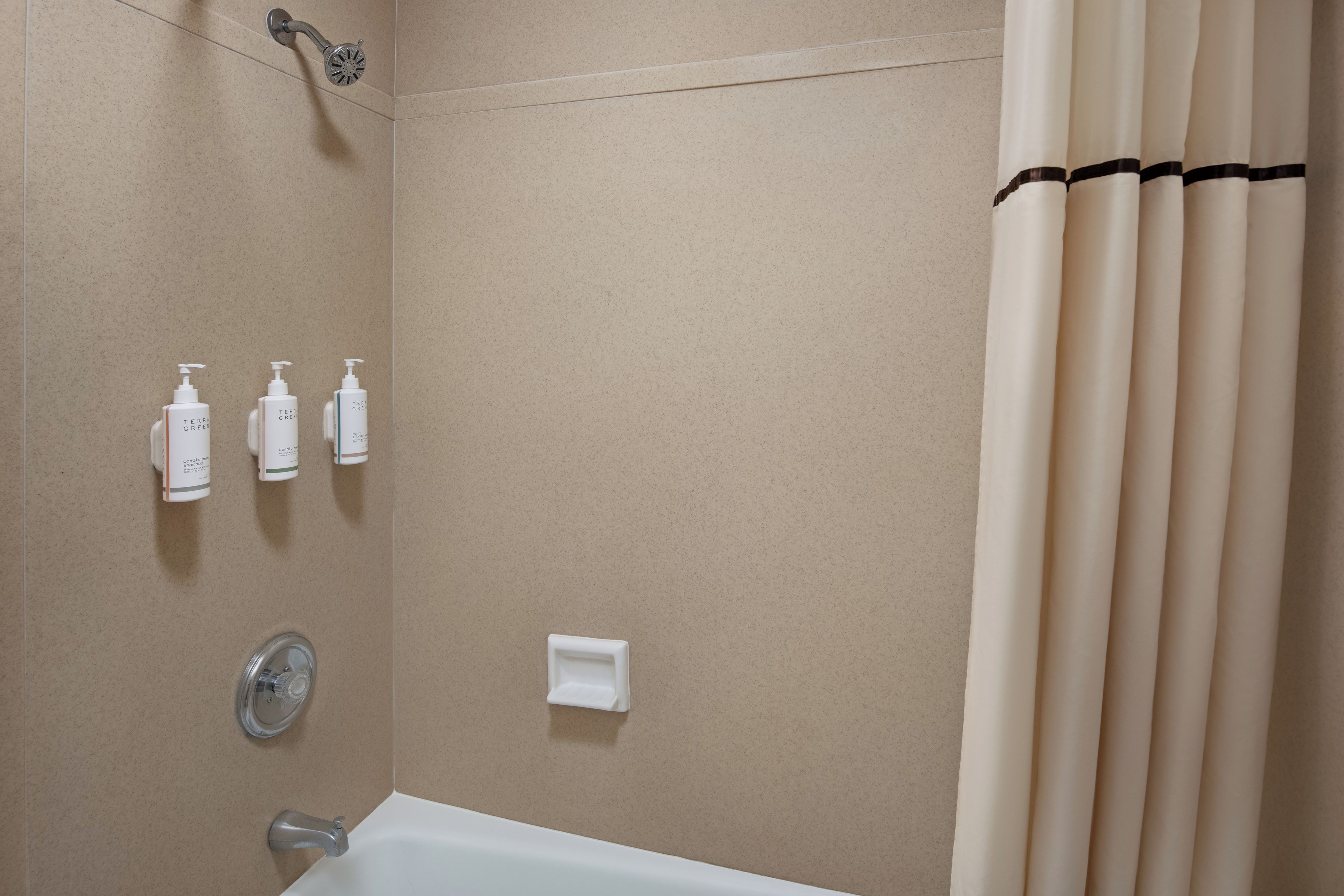 Une salle de bain équipée d’une baignoire, d’une douche et de trois distributeurs de savon placés sur le mur.