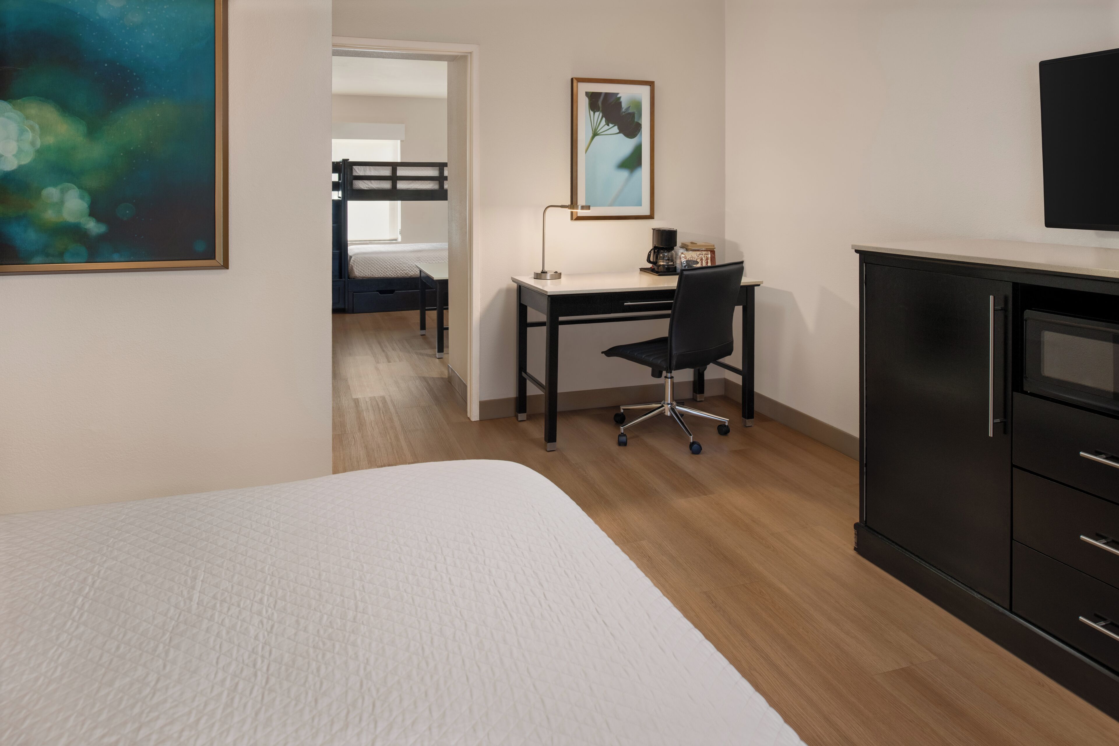 Un dormitorio con una cama, un escritorio, una silla, un aparador y un cuadro en la pared.