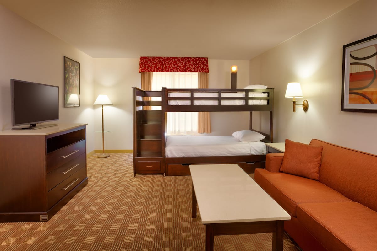 A hotel room with a bunk bed, a television, a desk, a sofa, and a lamp.