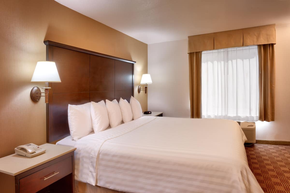 A hotel room with a large bed, two bedside lamps, a nightstand with a phone, and a window with curtains.