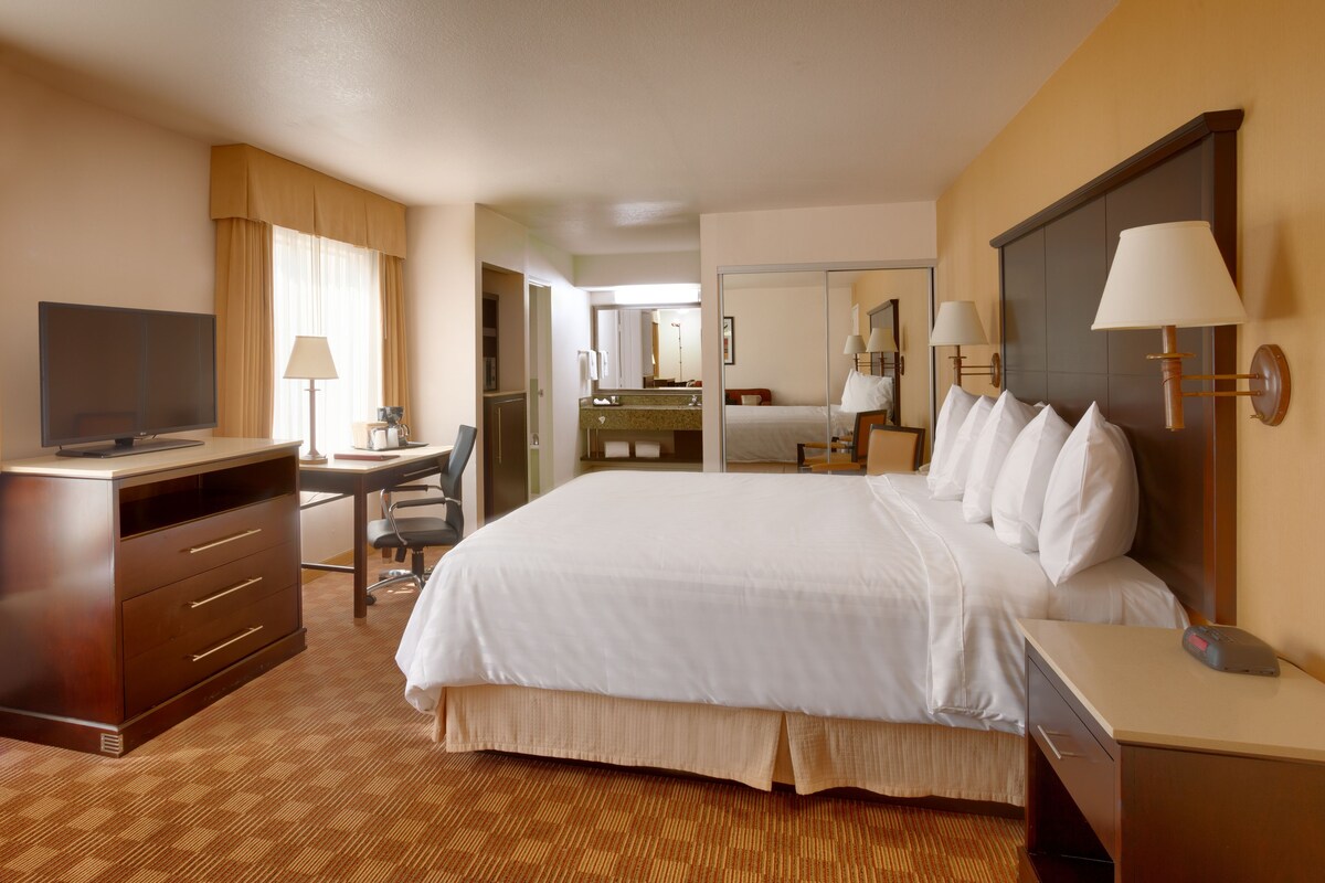 A hotel room with a bed, desk, TV, and a bathroom visible through an open door.