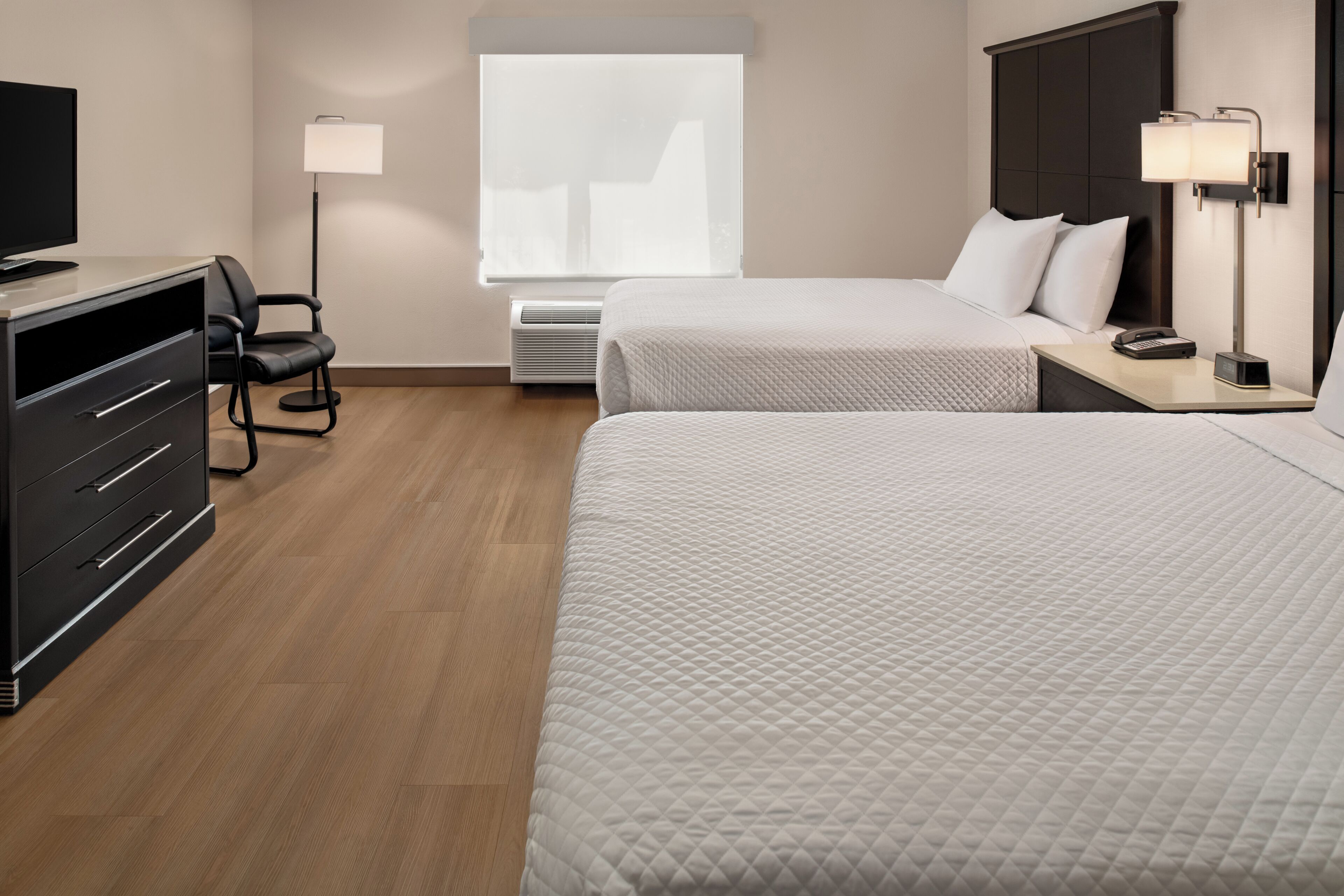Een hotelkamer met twee bedden, een bureau met stoel, een televisie en een raam met zonwering.