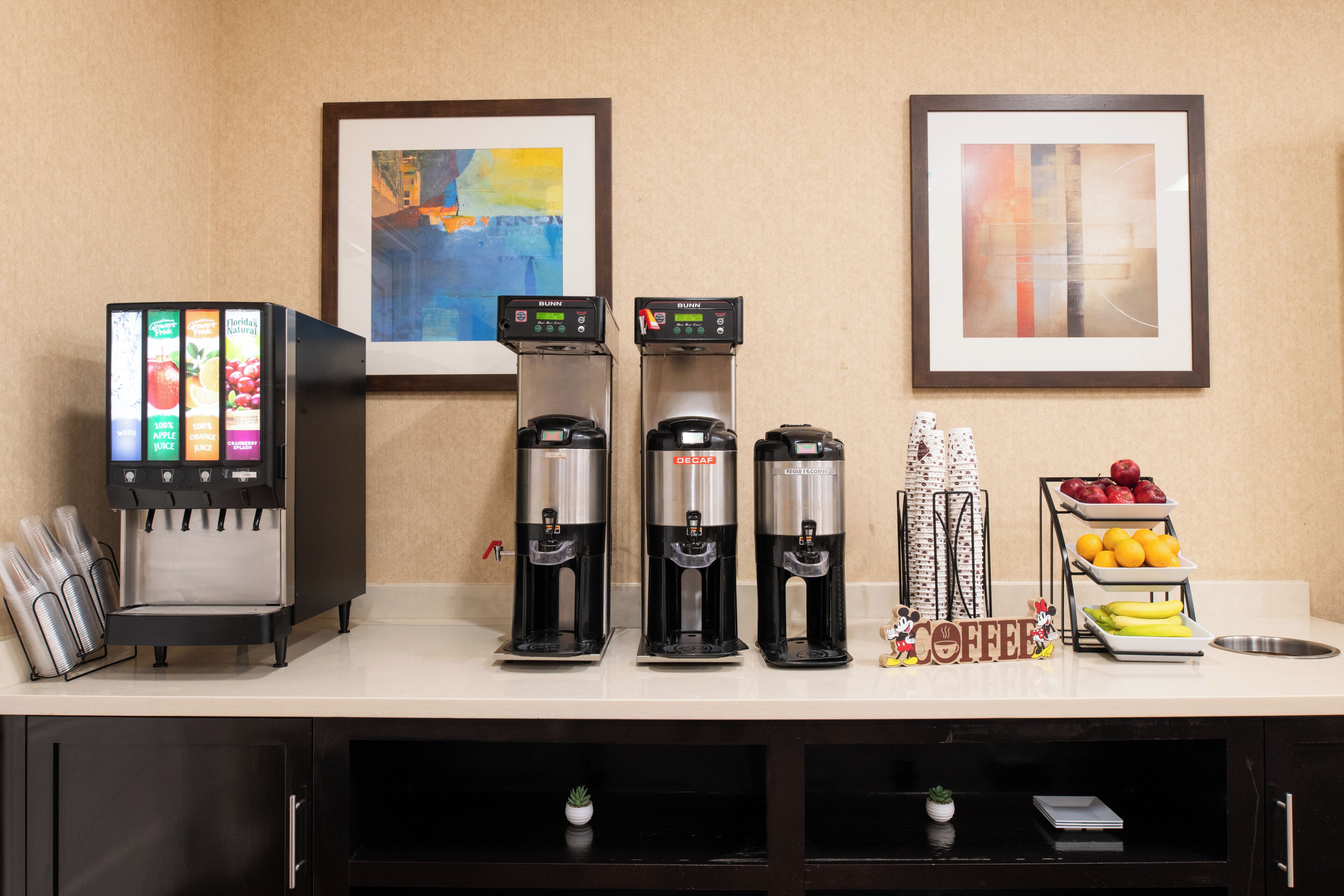 Un espace de libre-service proposant une variété de boissons, avec plusieurs distributeurs, une machine à café et un présentoir de fruits.
