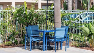A pool area with two blue chairs and a patterned umbrella, surrounded by a fence and greenery.