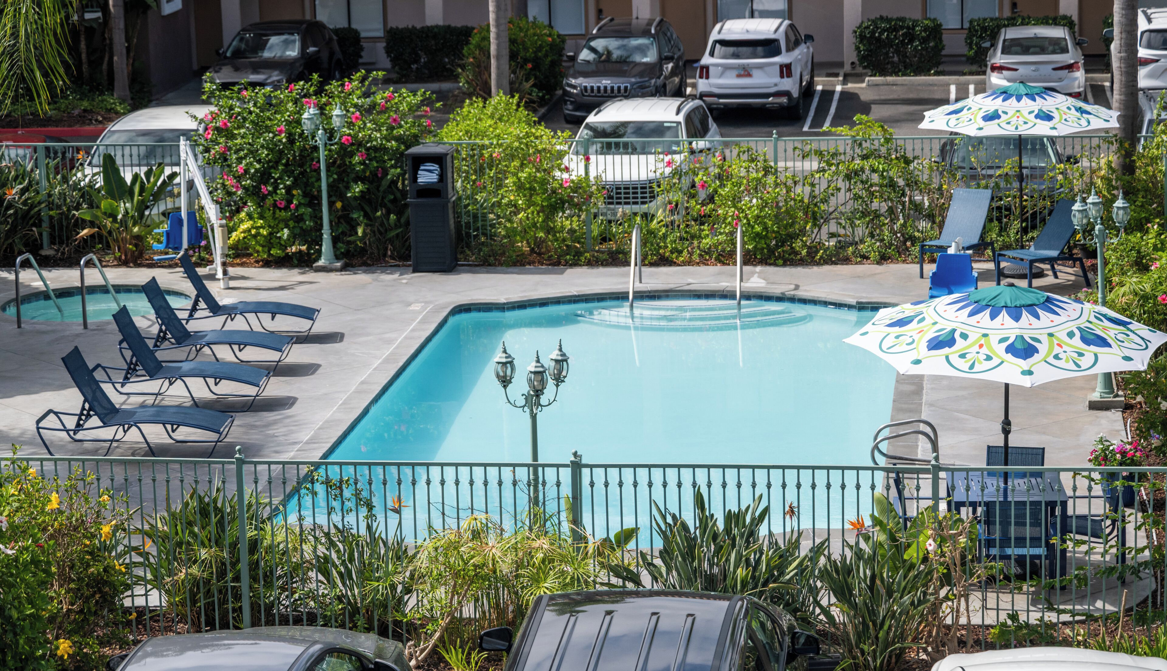 A swimming pool with lounge chairs and umbrellas, surrounded by a fence and greenery.