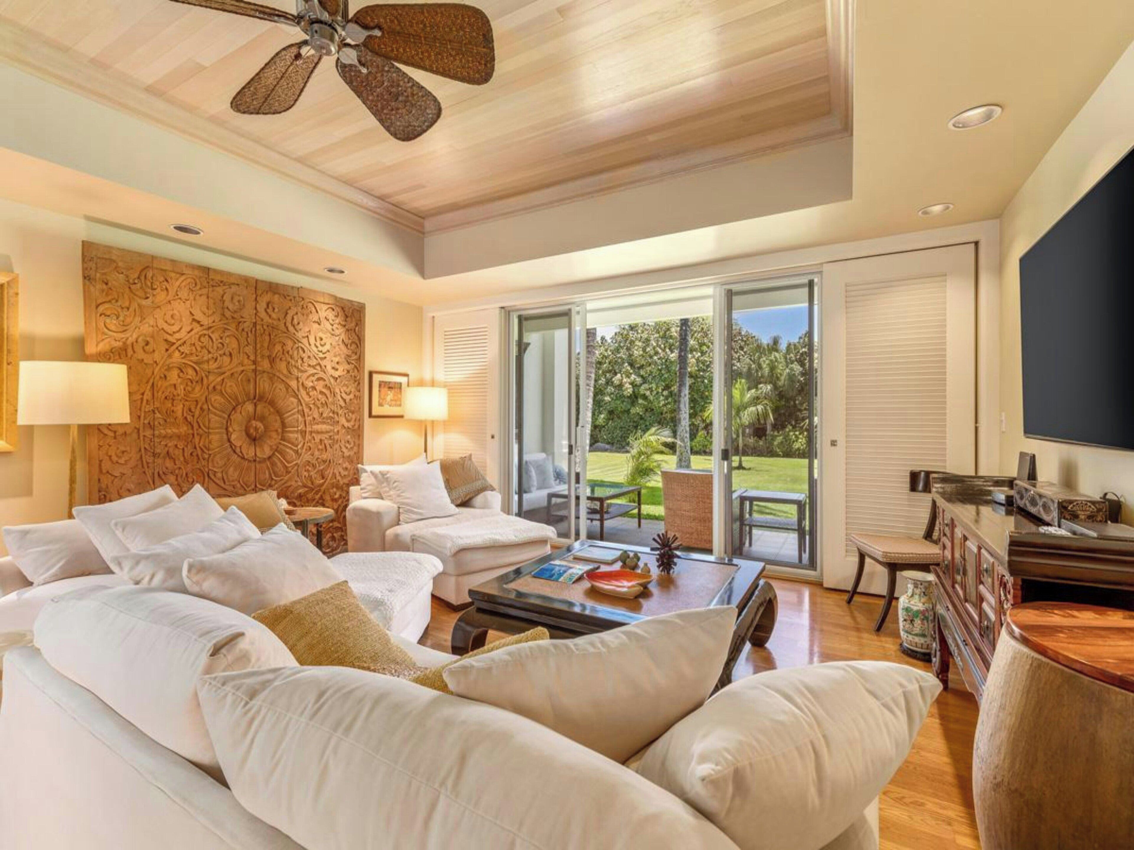 A spacious living room with a ceiling fan, a large sofa set, a coffee table, and a television.
