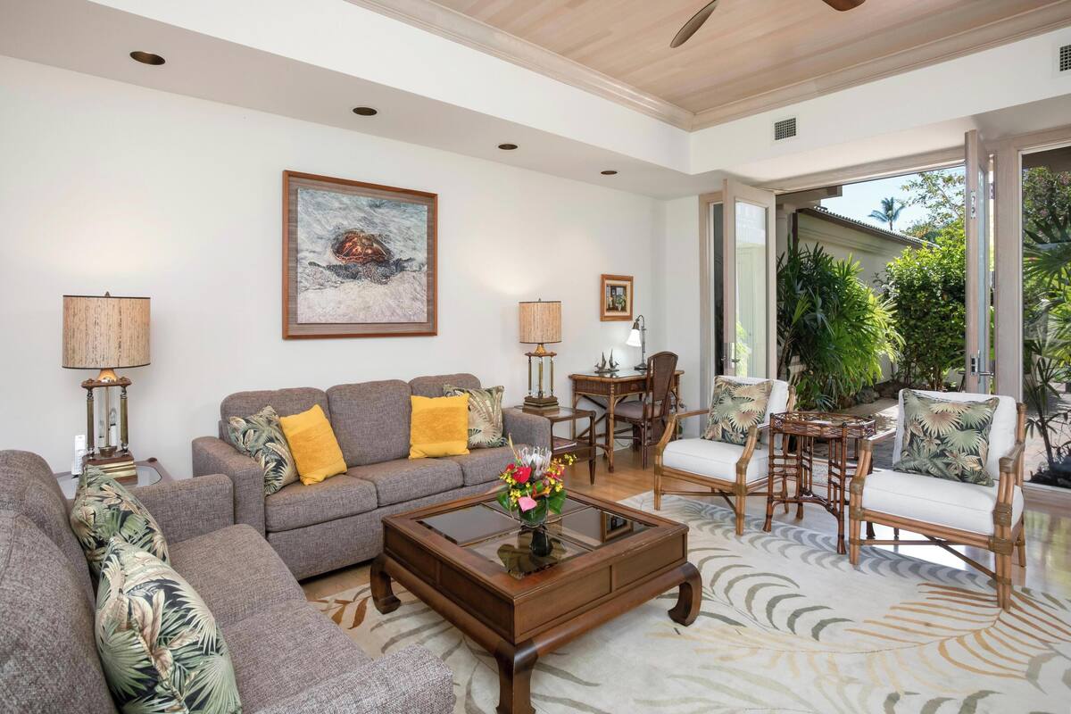 A spacious living room with a ceiling fan, a sofa set, a coffee table, and a dining area with chairs.