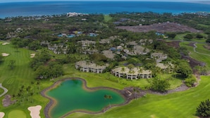 Un campo de golf con un estanque, rodeado de edificios residenciales y vistas al océano.