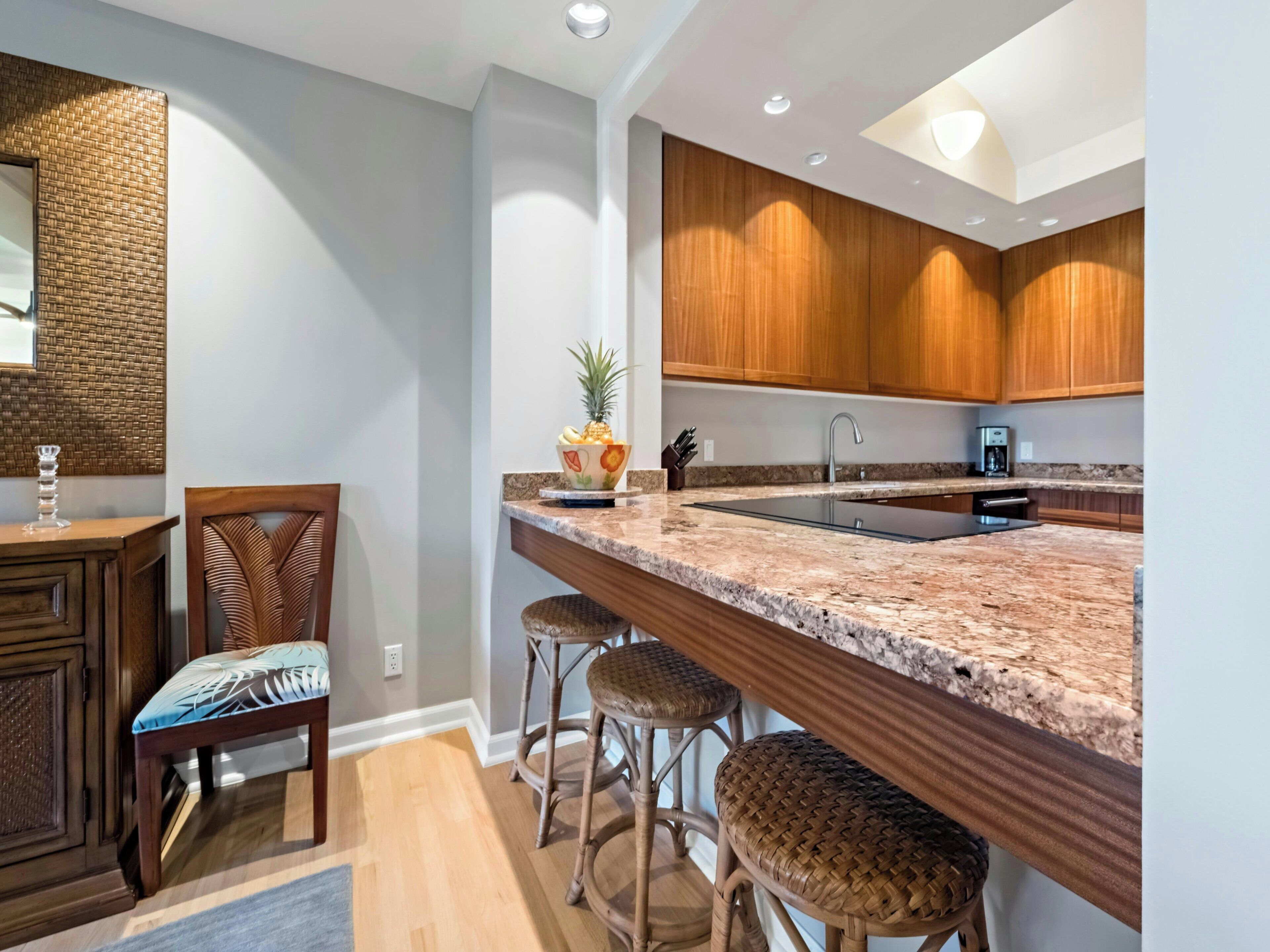 A modern kitchen with a granite countertop, wooden cabinets, a built-in island with bar stools, and a hanging light fixture.