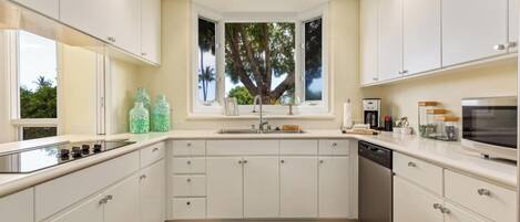 Una cocina moderna con armarios blancos, horno integrado y ventana con vistas a la vegetación.