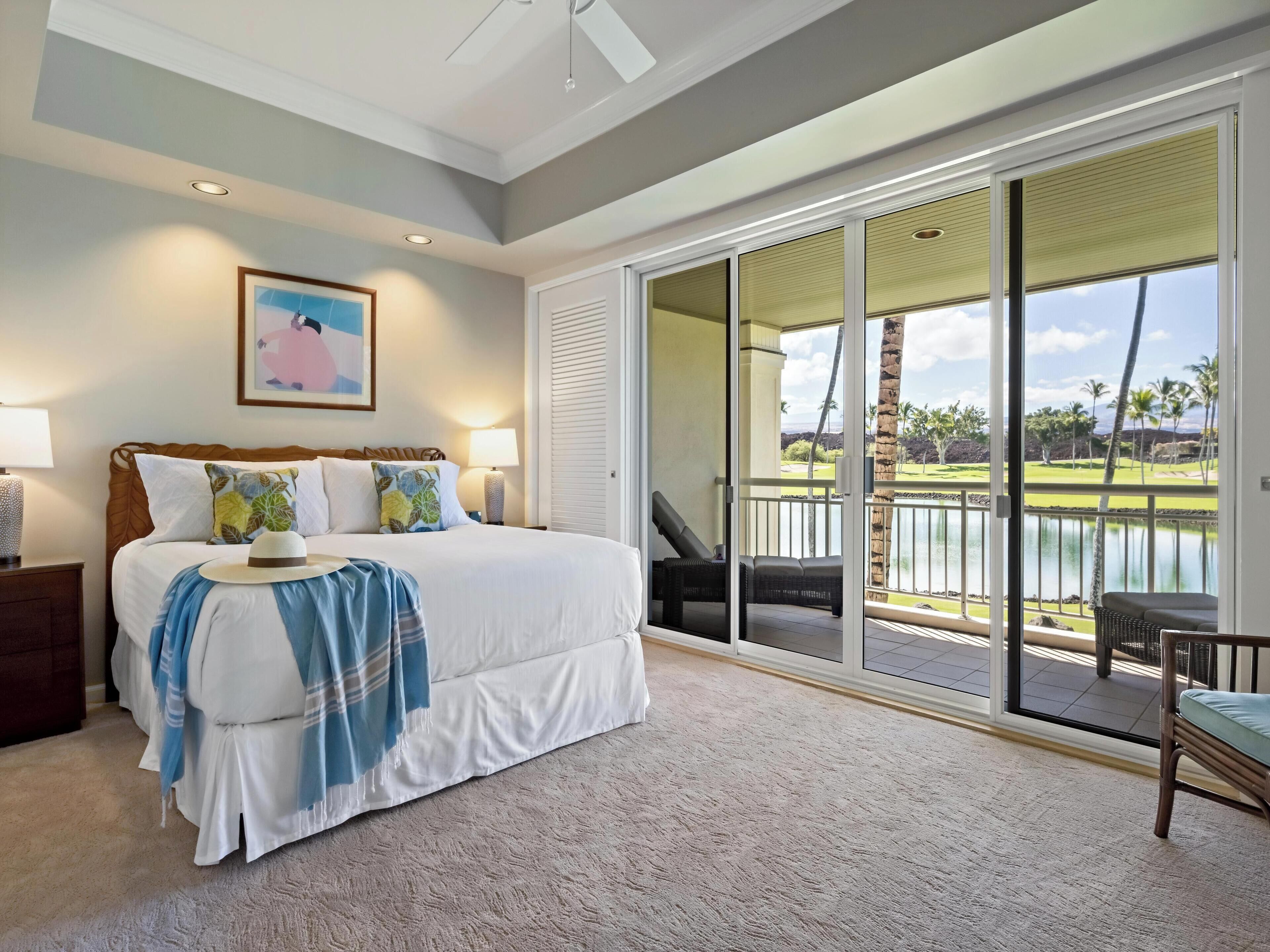 Een slaapkamer met een groot bed, uitzicht op een golfbaan en een schuifdeur naar een balkon.