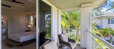 A balcony with wicker furniture, a bed with white bedding, and a ceiling fan.